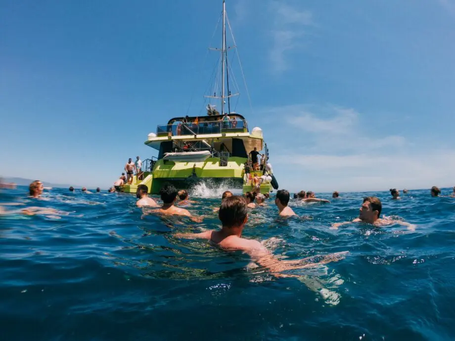 People swimming in the water beside a large catamaran in Barcelona